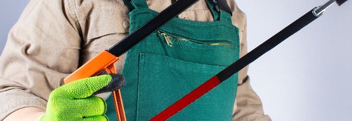 Arbeiters in grünem Overall mit Schutzhandschuhen und einer Bügelsäge